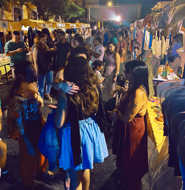 Movimento de pessoas entre as bancas da feira, à noite