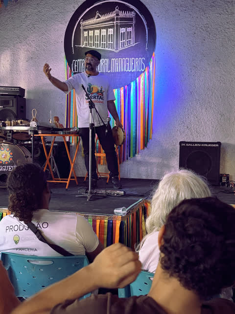 Apresentador no palco com o braço erguido diante da plateia