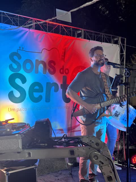 Guitarrista cantando diante do painel do Sons do Sertão