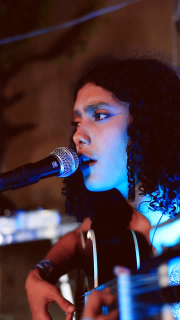 Cantora de cabelo cacheado tocando violão sob luz azul