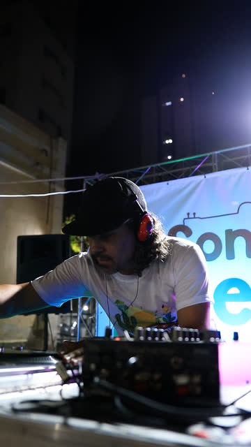 DJ na mesa de som diante do painel do Sons do Sertão
