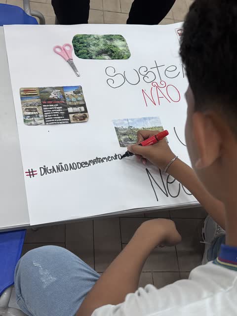 Estudante colando imagens num cartaz sobre sustentabilidade