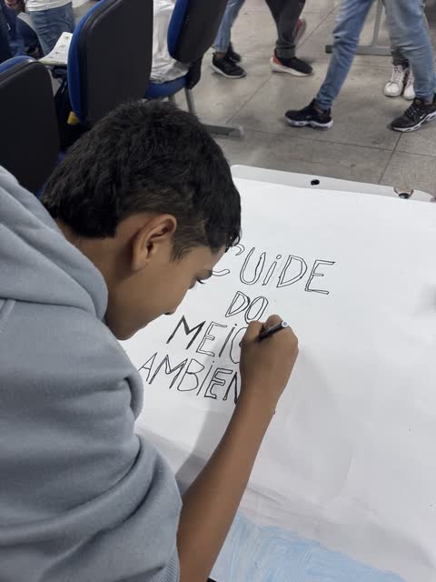 Estudante escrevendo Cuide do meio ambiente num cartaz
