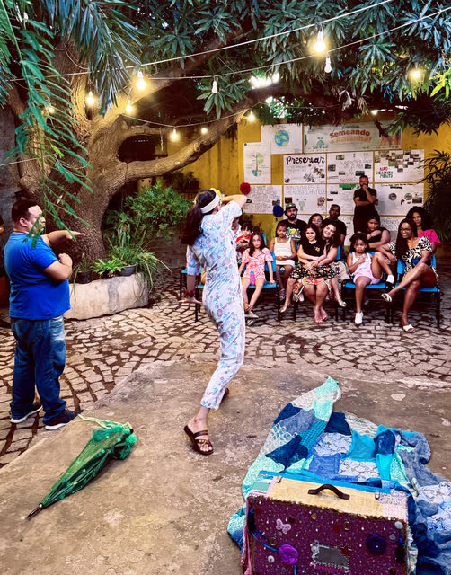 Atriz em cena diante de crianças e famílias sentadas no pátio